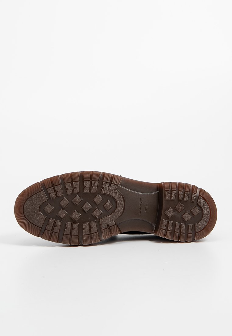 Semelle de chaussure en caoutchouc marron avec un motif texturé, présentant des rainures prononcées et des sections surélevées pour une meilleure adhérence et traction. Design plat et robuste.