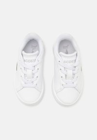 Vita sneakers i slät syntetiskt material, med rund tå, snörning och en grön logotypaccent på sidan.