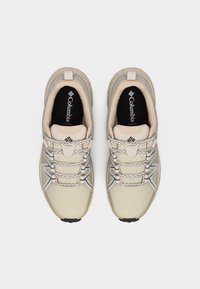 Ζευγάρι μπεζ αθλητικά παπούτσια Columbia με κορδόνια με σχέδια, διχτυωτό ύφασμα και μαύρες εσωτερικές σόλες, φαίνεται από πάνω σε λευκό φόντο.