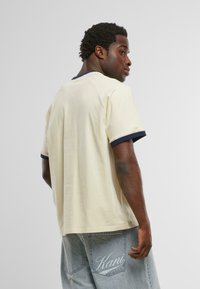 Krémové tričko s kulatým výstřihem a námořnickým modrým lemem. Volný střih, vyrobeno z měkké látky. Viditelné stehy v švech.