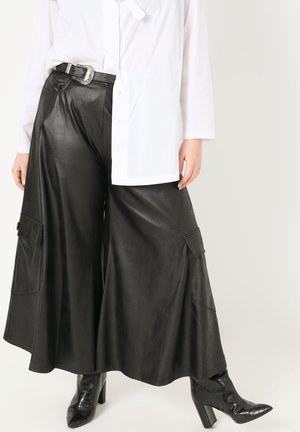 Zwarte neplederen wijde pantalon met twee zijzakken, gecombineerd met een witte overhemd. Zwarte gestructureerde enkelboots.