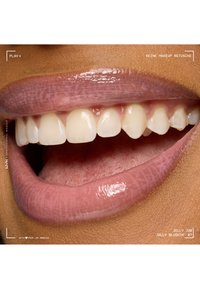 Lèvres mauves brillantes légèrement entrouvertes dévoilant des dents blanches et propres ainsi qu'une langue texturée sur une peau de ton brun moyen.