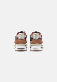 Zapatillas marrones y negras con acabado de gamuza, cuello acolchado y suela blanca con acentos marrones y un logo verde en el talón.