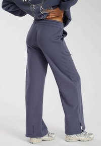 Grijze, lichte sweatpants met een elastische tailleband, rechte pijpen, zijzakken en een splitdetail aan de onderkant, gecombineerd met sport schoenen.