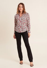 Blusa a maniche lunghe con sfondo bianco e motivo geometrico rosso e nero; presenta un colletto e chiusura con bottoni davanti.