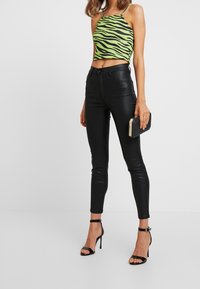 Grön zebra-mönstrad cropped topp med tunna axelremmar, tillsammans med tajta svarta läderbyxor och svarta remmar med stilettklackar.