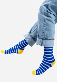 Niebiesko-białe skarpetki w paski z żółtymi palcami, noszone z podwiniętymi jasnoniebieskimi dżinsami, prezentujące swobodny styl.