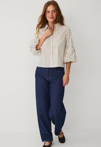 White button-up shirt with brown stripes, featuring ruffled bell sleeves. Paired with dark blue wide-leg jeans and black flats.