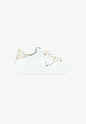 Baskets en cuir blanc avec un accent doré brillant au talon, semelle plate blanche et lacets dorés. Le panneau latéral présente une découpe triangulaire.
