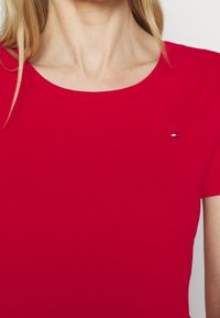 Rød bomulds t-shirt med korte ærmer og rund halsudskæring. Har et lille logo på den øverste venstre side. Glat tekstur.