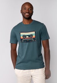 Teal T-shirt met korte mouwen, voorzien van een retro cassettebandje grafiek met kleurrijke strepen en zwarte details, gecentreerd op de borst.