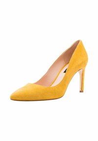 Zapato de tacón alto de ante amarillo con puntera afilada y un tacón delgado y transparente. El interior presenta un forro beige y un diseño minimalista.