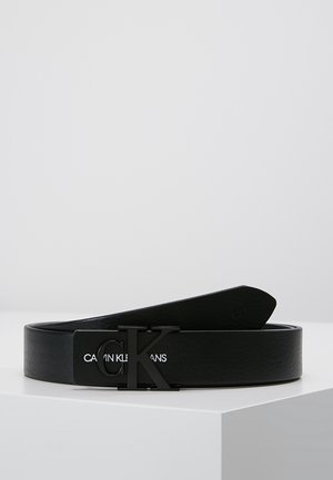 Czarny skórzany pasek Calvin Klein z czarną metalową klamrą z logo "CK", umieszczony na białej powierzchni na jednolitym tle.