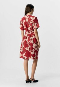 Rød blomstermønstret kjole i let stof, knælængde, med korte ærmer og bæltet i taljen. Sorte slingback sko.