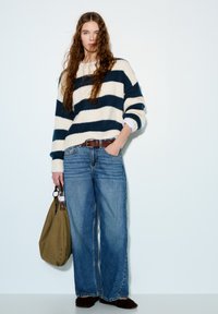 Pruhovaný pletený svetr v krémové a námořnické modré, široké modré džíny, hnědý pásek, olivově zelená kabelka a hnědé chlupaté boty.