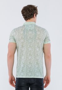 Camiseta polo verde de manga corta con un patrón texturizado, cuello y mangas rematadas, mostrada en un modelo visto desde la espalda.