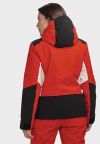 Rote und schwarze isolierte Outdoor-Jacke mit abnehmbarer Kapuze, ausgestattet mit weißen Akzenten und einer figurnahen Passform. Weiche Textur und strukturierte Form.