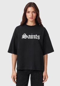 Zwarte oversized t-shirt gemaakt van een zachte katoenen mix, met gedurfde witte tekst "Saints" in een gestileerd lettertype op de borst.