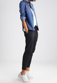 Denimskjorta med långa ärmar, mörkgrå joggingbyxor och vita sneakers. Skjortan har knäppning och bröstfickor. Mjuk textur hela vägen igenom.