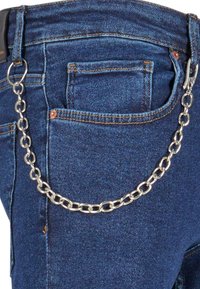 Denim traperice s metalnom srebrnom lancem zakačenom na petlju za pojas, klasične plave boje i standardnim džepovima, blago izblijedjelom teksturom.