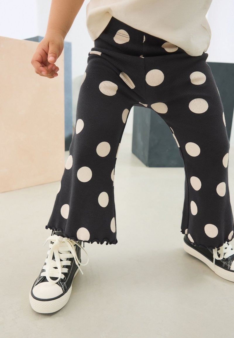 Schwarze gerippte ausgestellte Hose mit großen cremefarbenen Polka-Dots, mit einem Rüschensaum versehen und kombiniert mit schwarz-weißen Sneakers.