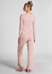 Roze loungewear set met een geribbelde lange mouw top en bijpassende broek met een ontspannen pasvorm, gecombineerd met zachte roze slippers.
