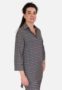 Blusa de patrón en blanco y negro con cuello tipo polo, mangas tres cuartos y corte recto. Tela suave con un diseño geométrico.