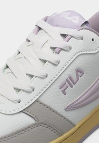 Λευκό πάνινο παπούτσι FILA με ανοιχτό μοβ λεπτομέρειες, χοντρά λευκά κορδόνια, υφή δέρματος και μπεζ σόλα.