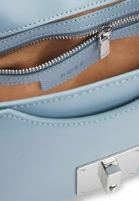 Borsa a tracolla in pelle azzurro chiaro con finitura liscia, dotata di una cerniera argentata, fodera interna in suede e chiusura a morsetto metallica.