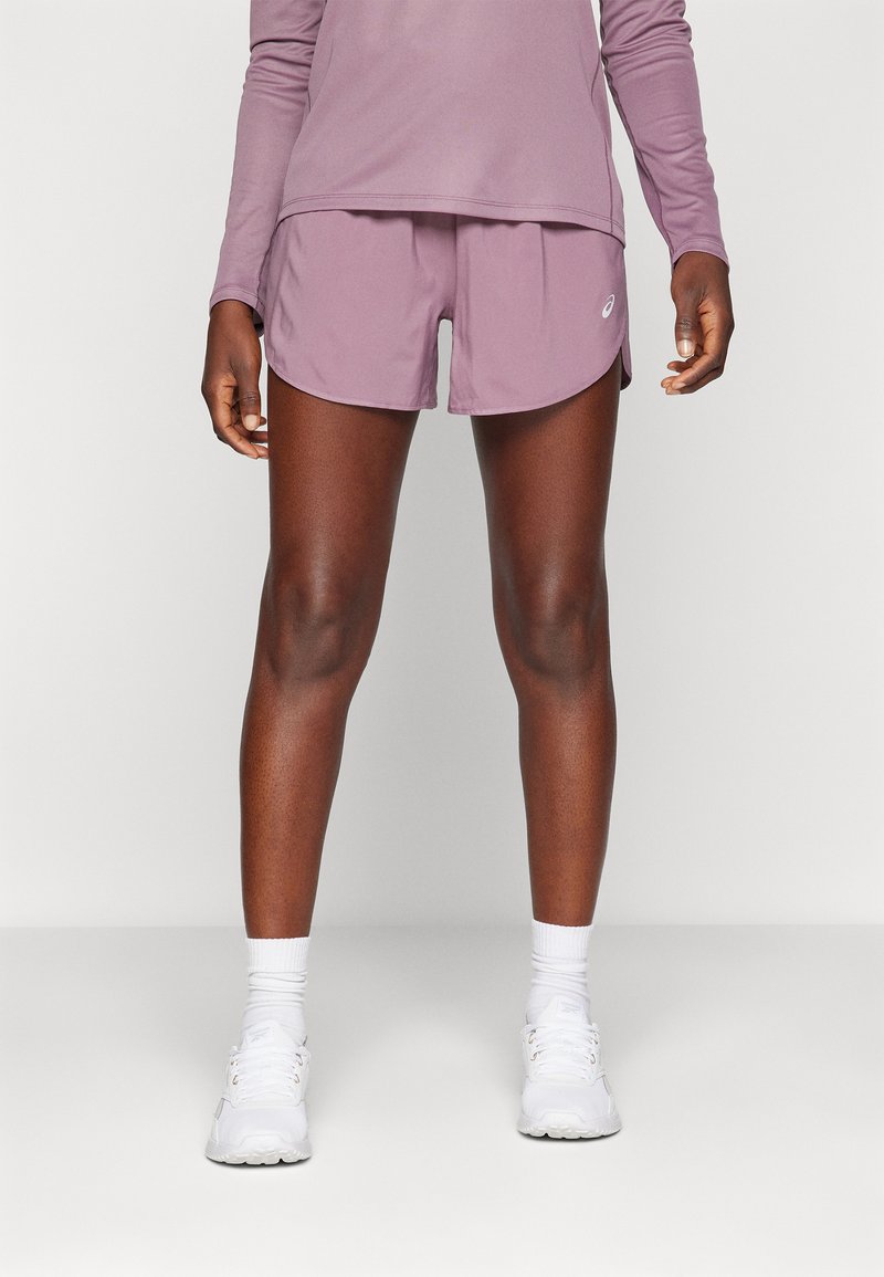 Krátké levandulové sportovní šortky s hladkým povrchem, bočními rozparky a detailem loga. Kombinované s bílými ponožkami a botami, pod dlouhým rukávem.