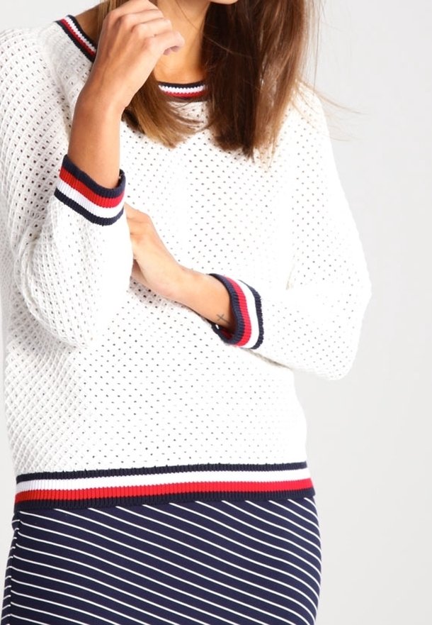Maglione bianco a maglia con una trama aperta e testurizzata, con righe navy e rosse a costine sul colletto, sui polsini e sull'orlo. Abbinato a una gonna a righe navy.