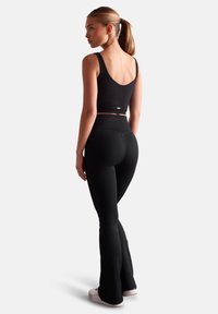 Black ribbed crop top with thin straps paired with black flared leggings. Textured fabric with a fitted design and a smooth finish.