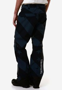 Pantaloni da sci neri con strisce diagonali grigio scuro, dotati di un logo sulla parte inferiore della gamba, orli rinforzati e diverse tasche.