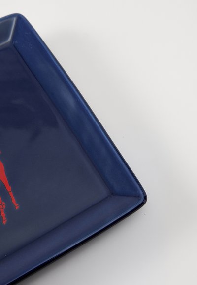 Négyzet alakú, kék kerámia tányér fényes felülettel, amelynek tetején egy piros grafikai ábra látható. Éles, szögletes sarkok.