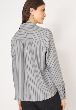 Chemise grise à manches longues avec des rayures verticales noires. Elle possède un col et des poignets à boutons, avec une coupe légèrement décontractée et un tissu texturé.