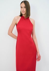 Rød halterneck-kjole lavet af glat stof, med en tætsiddende overkrop og en flydende silhuet. Minimalistisk design uden synlige mønstre.