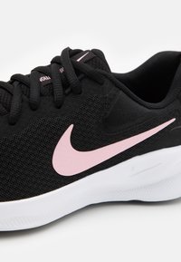 Scarpa da ginnastica nera con tomaia in rete, accentuata da un logo Nike rosa, lacci piatti e suola bianca testurizzata. Dettaglio ravvicinato che mette in evidenza i particolari del design.