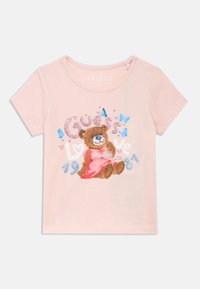 Ροζ βαμβακερό T-shirt με απεικόνιση αρκούδας που φορά φιόγκο. Περιλαμβάνει λαμπερό κείμενο "Guess Love 1981" και μικρές διακοσμήσεις πεταλούδας. Κοντά μανίκια.