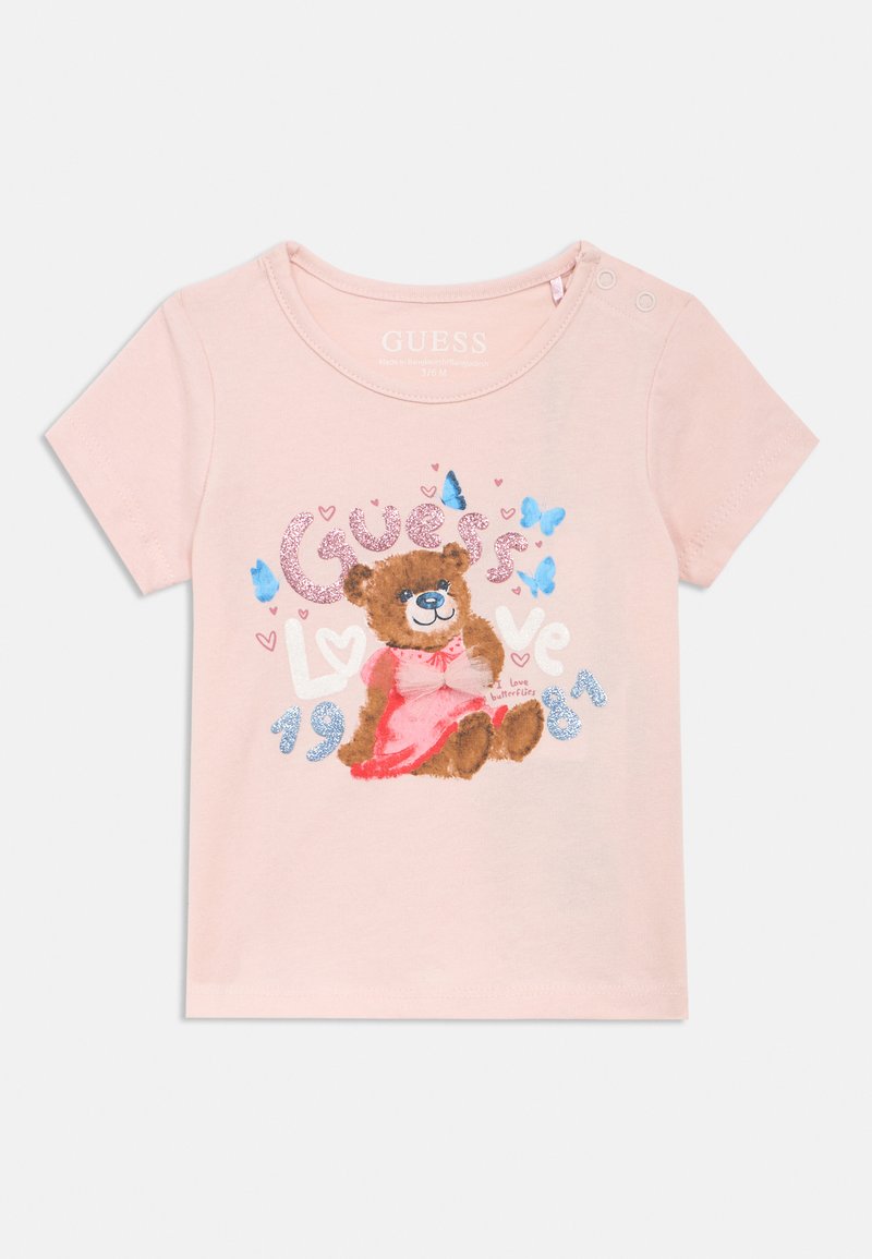 T-shirt en coton rose avec une illustration d'ours portant un nœud. Comprend un texte scintillant "Guess Love 1981" et de petits accents de papillons. Manches courtes.