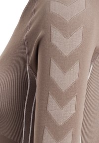 Gros plan sur un tissu tricot taupe montrant une manche avec quatre grands motifs en chevrons et une texture côtelée sur la partie latérale.