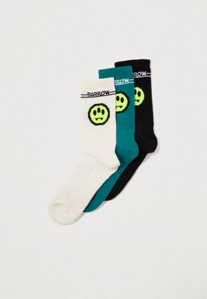 Tre paia di calzini a coste: bianchi con un faccione sorridente verde, verde acqua con un faccione sorridente verde e neri con dettagli verdi.