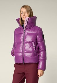 Purple puffer jacket with a high collar, zip closure, side pockets, and black circular accent on sleeve. Glossy finish and quilted design.