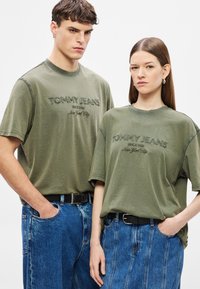 Tricouri din bumbac verde măsliniu cu logo-ul "TOMMY JEANS" brodat, asortate cu blugi din denim albastru cu talie înaltă și cusături vizibile.