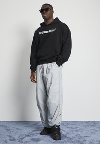 Black hoodie with "forgotten faces" text, gray lightweight baggy pants, and black shoes. Smooth fabric with ribbed cuffs and elastic waistband.