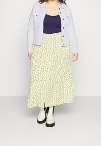 Ljusgul blommig kjol med svarta detaljer, kombinerad med en marinblå topp och en grå jacka. Skor är vita ankelstövlar med svarta sulor.