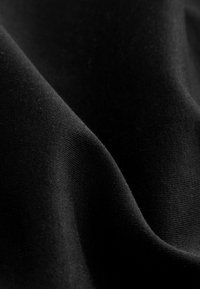 Sort stof med en glat tekstur, der viser subtile folder og en ensartet overflade. Materialet virker blødt og let.