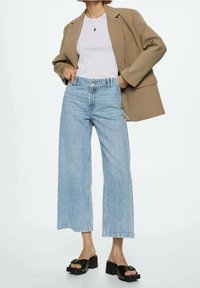 Jeans de tiro alto de mezclilla en un tono azul claro, combinados con una camiseta blanca ajustada y un blazer beige de gran tamaño. Sandalias de plataforma negras.