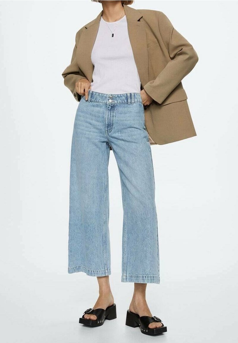 Jeans de tiro alto de mezclilla en un tono azul claro, combinados con una camiseta blanca ajustada y un blazer beige de gran tamaño. Sandalias de plataforma negras.