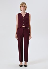 Completo bordeaux a due pezzi composto da un gilet aderente senza maniche con scollatura a V e bottoni circolari, abbinato a pantaloni eleganti a vita alta.