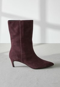 Burgundské semišové členkové topánky s ostrou špičkou, úzkym opätkom a jemnými detailmi v šve. Hladká textúra s elegantným, priliehavým dizajnom.